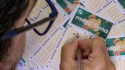 Apostador de óculos preenche com caneta volantes da Mega-Sena espalhados sobre uma mesa; imagem de arquivo