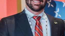 Eduardo Bolsonaro em evento político, sorrindo e vestindo terno