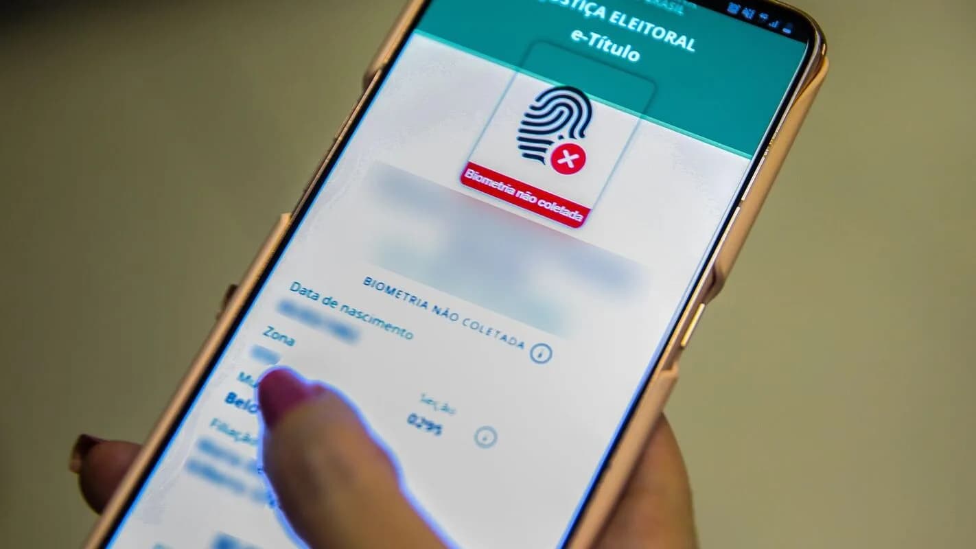 Mão segura celular com aplicativo eleitoral do TSE aberto na tela