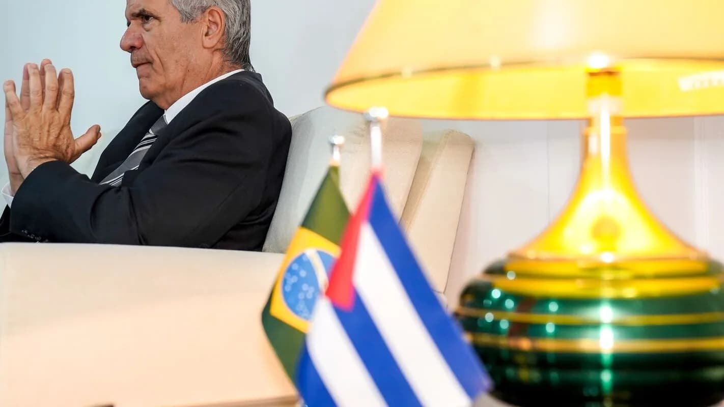 Embaixador de Cuba no Brasil, Victor Manuel Cairo Palomo, sentado em entrevista com bandeiras do Brasil e de Cuba ao fundo