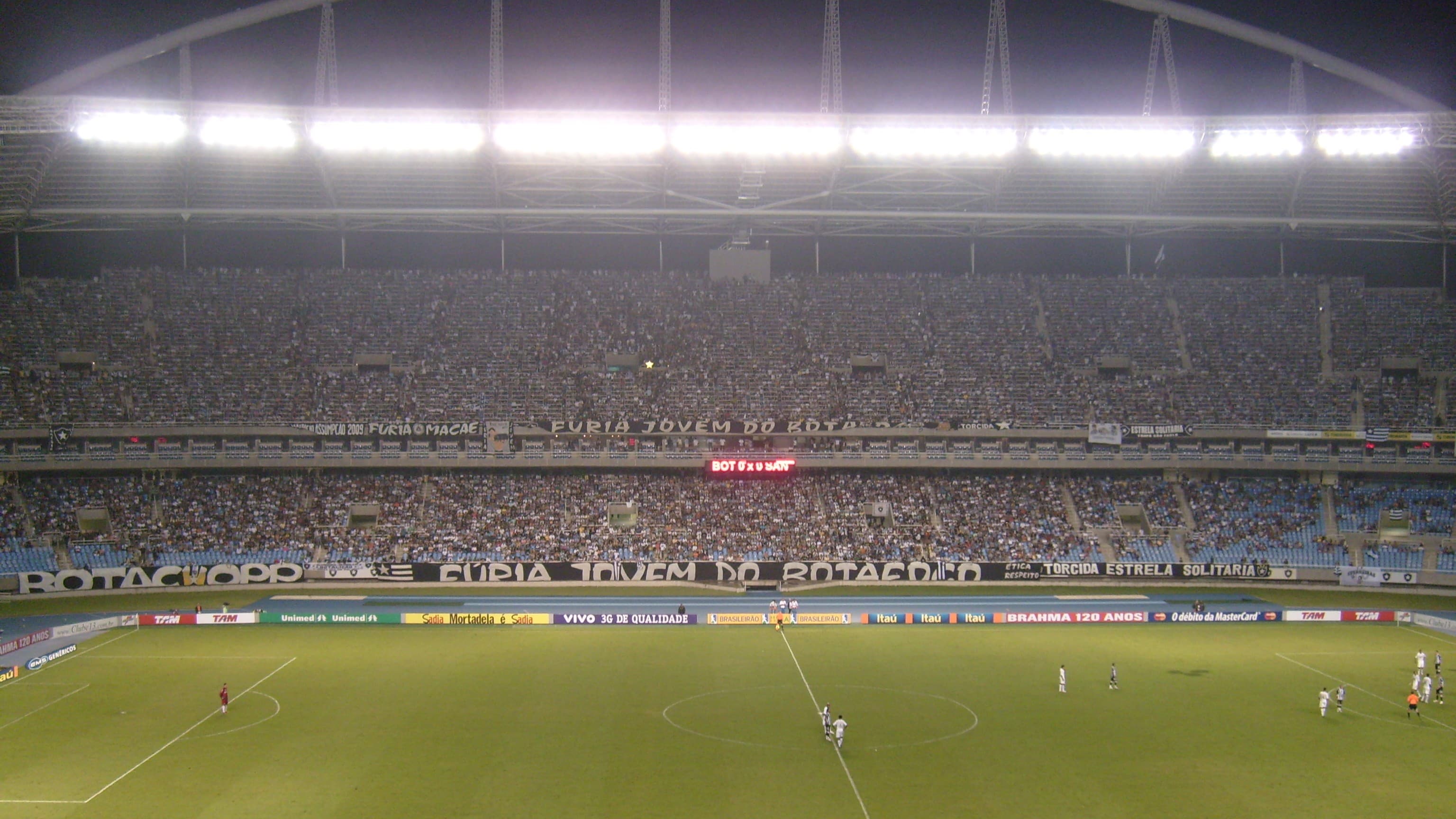 Estádio Nilton Santos lotado durante partida do Botafogo à noite, com faixas da torcida (foto de arquivo)