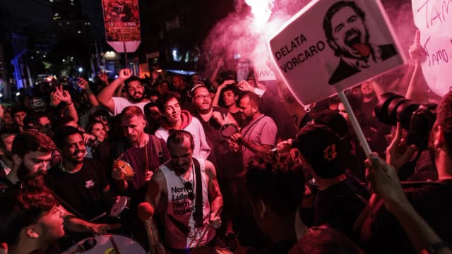 Manifestantes protestam contra o Banco Master à noite, com cartaz caricato de Daniel Vorcaro