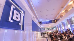 Painel com o logo da B3 na sede da bolsa de valores em São Paulo, com público sentado ao fundo