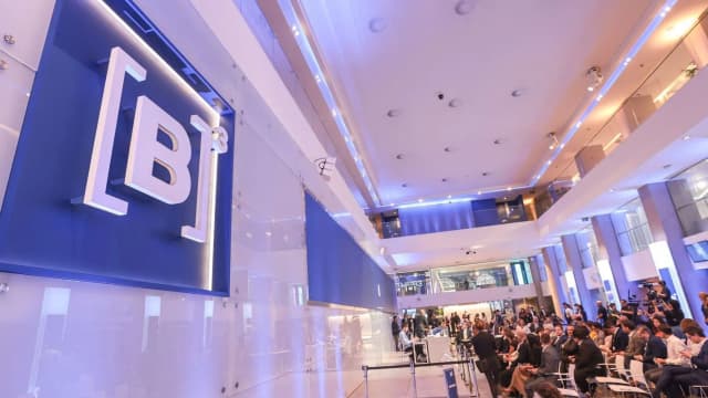 Painel com o logo da B3 na sede da bolsa de valores em São Paulo, com público sentado ao fundo