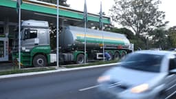 Caminhão-tanque descarrega combustível em posto de Brasília, em imagem de arquivo, enquanto um trabalhador opera a mangueira e um carro passa pela avenida