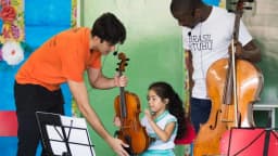 Educador toca violino com uma criança em sala de aula de escola pública