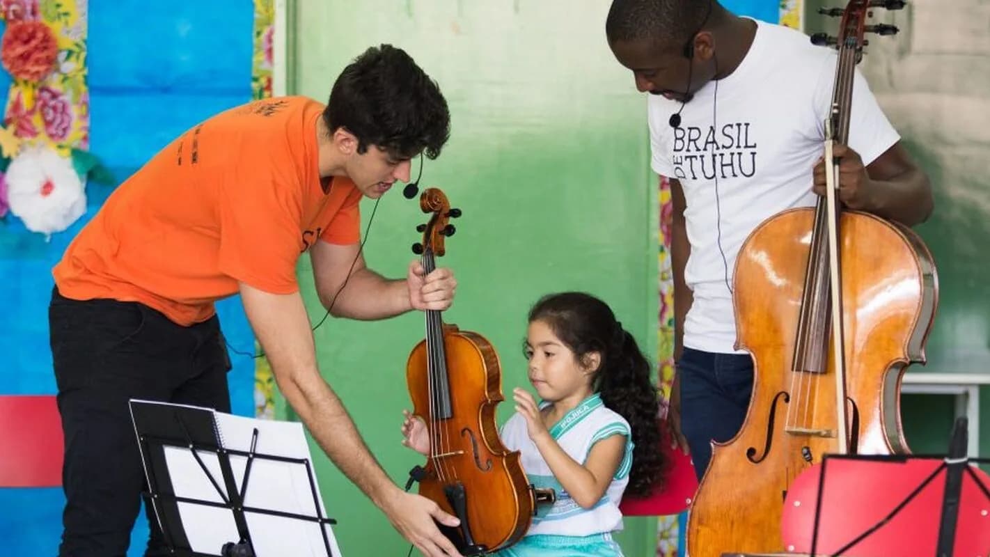 Educador toca violino com uma criança em sala de aula de escola pública