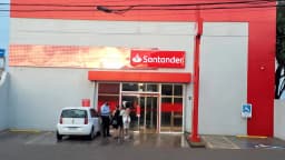 Fachada de agência do Santander com clientes em frente