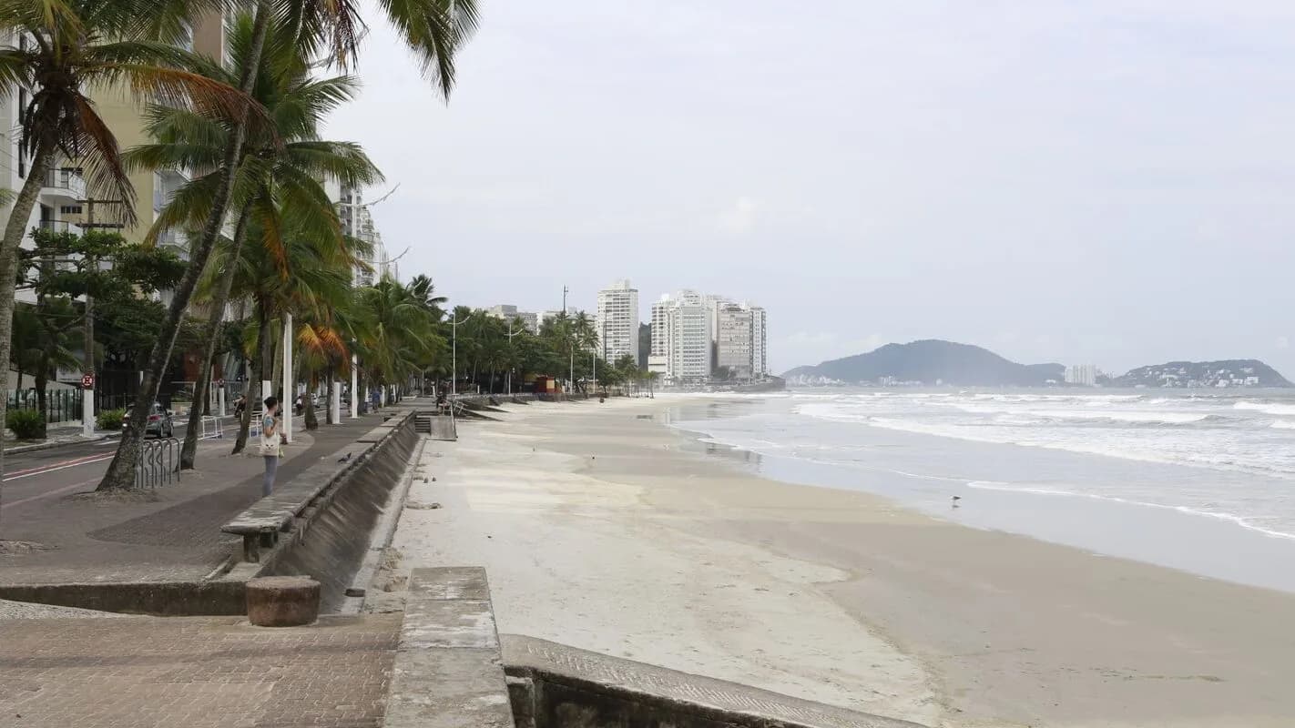Orla de praia no litoral de São Paulo, com calçadão e prédios ao fundo