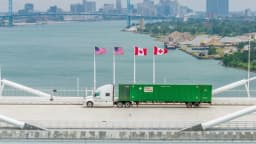 Caminhão de carga cruza ponte de fronteira entre Estados Unidos e Canadá, com bandeiras dos dois países