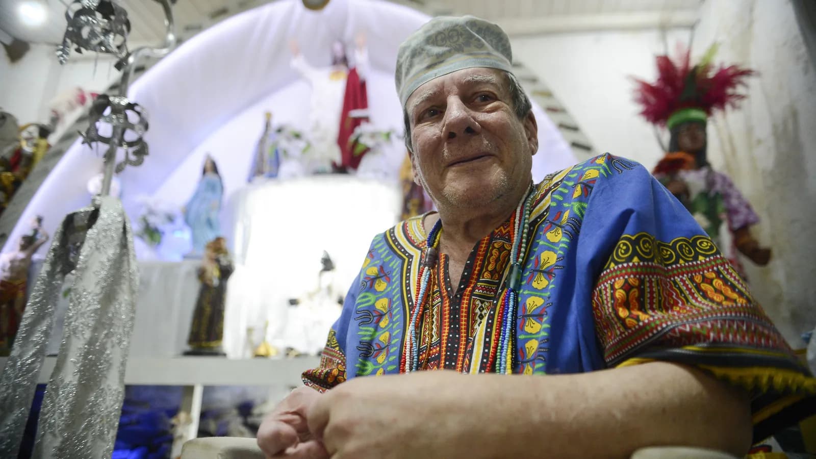 Praticante de Umbanda em terreiro, cercado por imagens religiosas