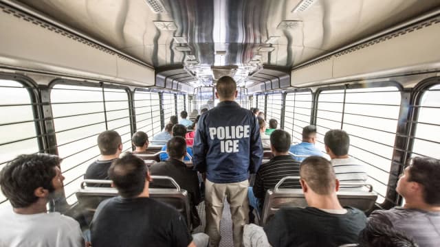 Agente do ICE escolta imigrantes detidos dentro de um ônibus rumo a um centro de detenção