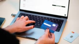 Pessoa faz compra online segurando cartão bancário em frente a um notebook