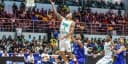 Jogador da seleção brasileira de basquete arremessa ao gol durante partida das Eliminatórias, com defensor da Venezuela tentando bloquear