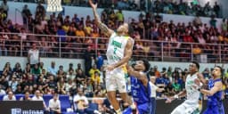 Jogador da seleção brasileira de basquete arremessa ao gol durante partida das Eliminatórias, com defensor da Venezuela tentando bloquear