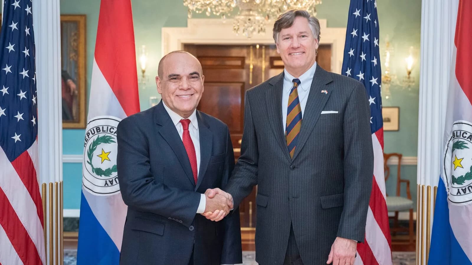 Christopher Landau, subsecretário de Estado dos EUA, aperta a mão de autoridade paraguaia diante das bandeiras dos dois países