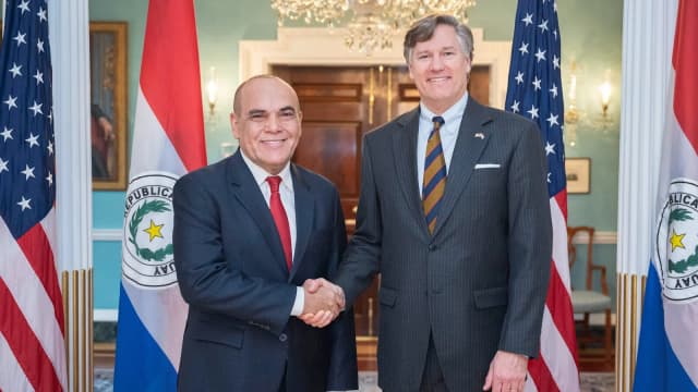 Christopher Landau, subsecretário de Estado dos EUA, aperta a mão de autoridade paraguaia diante das bandeiras dos dois países