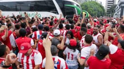 Torcedores do Náutico vestindo camisas rubro-brancas aglomerados em frente a ônibus do clube