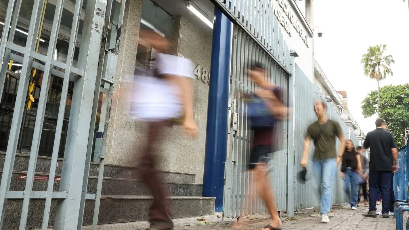 Pessoas caminham em frente a prédio onde ocorre prova de concurso, foto de contexto