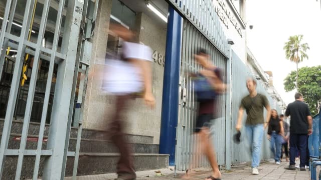 Pessoas caminham em frente a prédio onde ocorre prova de concurso, foto de contexto