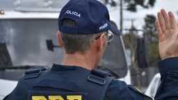 Agente da Polícia Rodoviária Federal de costas, fazendo sinal com a mão em fiscalização de rotina em rodovia (foto de arquivo)