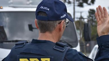 Agente da Polícia Rodoviária Federal de costas, fazendo sinal com a mão em fiscalização de rotina em rodovia (foto de arquivo)