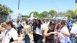 Grupo de estudantes adultos caminha em área externa de um local de provas, em dia de sol; imagem de arquivo