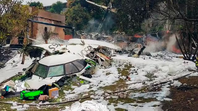 Destroços do avião da Voepass cobertos de espuma de combate a incêndio, com bombeiros ao fundo, em Vinhedo (SP)