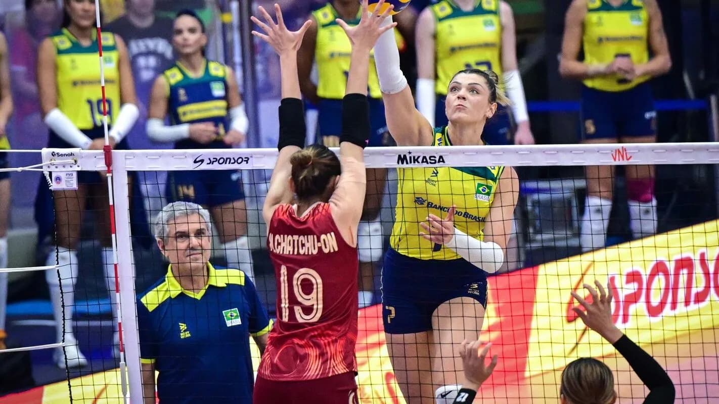 Jogadoras da seleção brasileira feminina de vôlei em ação na rede, com a comissão técnica ao fundo