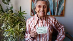 Mulher idosa segura documento em casa, geração que mais tem valores a receber do antigo PIS/Pasep