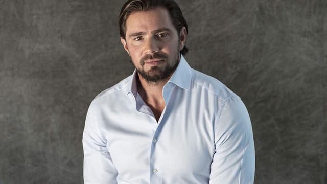 Retrato de divulgação do ex-banqueiro Daniel Vorcaro, de camisa social azul-clara, diante de fundo cinza