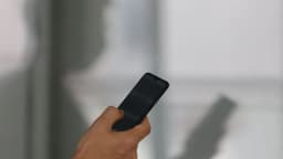 Mão segurando um celular ao acessar um aplicativo, em referência às apostas on-line