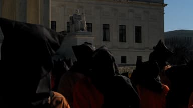 Manifestantes usam capuzes pretos e macacões laranja em ato pelo fechamento da prisão de Guantánamo em frente à Suprema Corte dos EUA