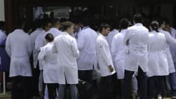 Candidatos de jaleco branco aguardam em fila para entrar em sala de prova de concurso público da área da saúde