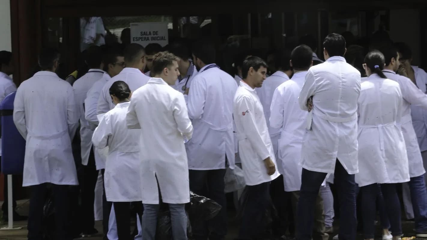 Candidatos de jaleco branco aguardam em fila para entrar em sala de prova de concurso público da área da saúde