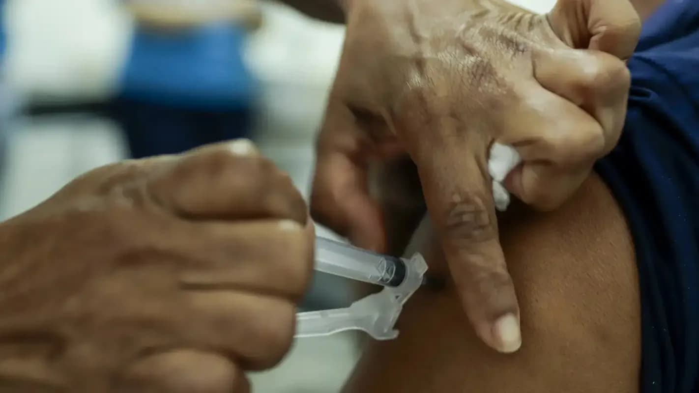 Profissional de saúde aplica injeção no braço de paciente, em imagem de contexto sobre atendimento de saúde
