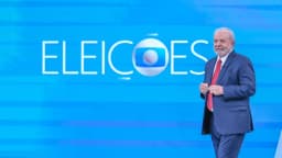 Lula em pé diante do logotipo Eleições da TV Globo em estúdio de debate presidencial anterior