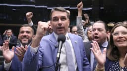 Flávio Bolsonaro discursa ao microfone cercado por parlamentares aliados comemorando
