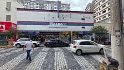 Fachada de uma loja da rede Casas Bahia em rua de comércio, com pedestres passando em frente