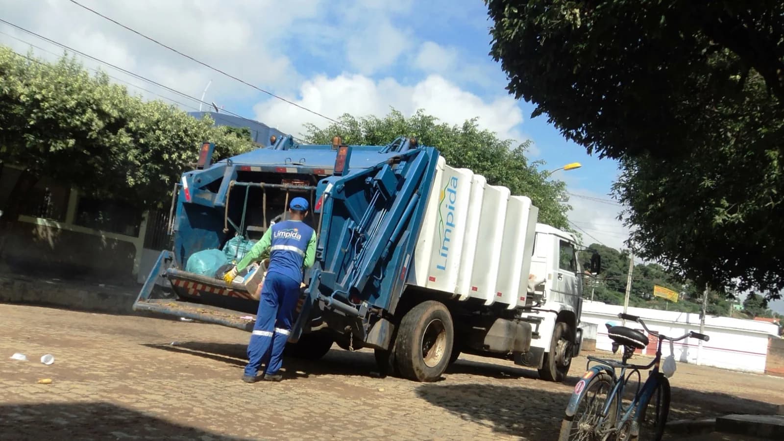 Gari trabalhando na coleta de lixo ao lado de um caminhão compactador em rua brasileira