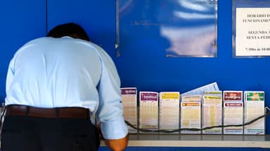 Homem de costas consulta volantes de apostas da Mega-Sena e outras loterias em balcão de casa lotérica