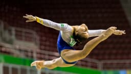 Flávia Saraiva durante salto no ar em apresentação de ginástica artística, com uniforme da seleção brasileira