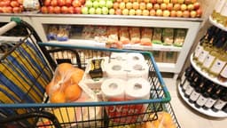 Carrinho de supermercado com alimentos e produtos de limpeza em corredor de hortifruti