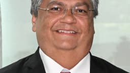 Retrato do ministro Flávio Dino, de terno escuro e óculos, sorrindo
