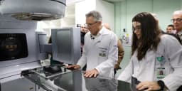 Ministro Alexandre Padilha, de jaleco branco, examina equipamento médico ao lado de uma profissional de saúde durante visita a hospital universitário