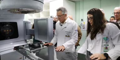 Ministro Alexandre Padilha, de jaleco branco, examina equipamento médico ao lado de uma profissional de saúde durante visita a hospital universitário