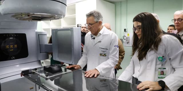 Ministro Alexandre Padilha, de jaleco branco, examina equipamento médico ao lado de uma profissional de saúde durante visita a hospital universitário