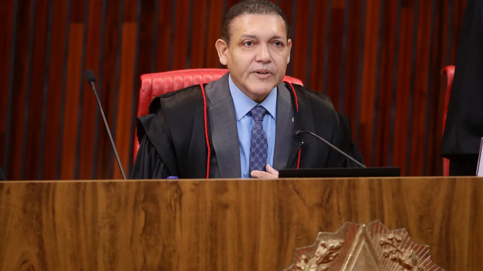 Ministro do TSE preside sessão plenária do tribunal, com o brasão da Justiça Eleitoral em primeiro plano