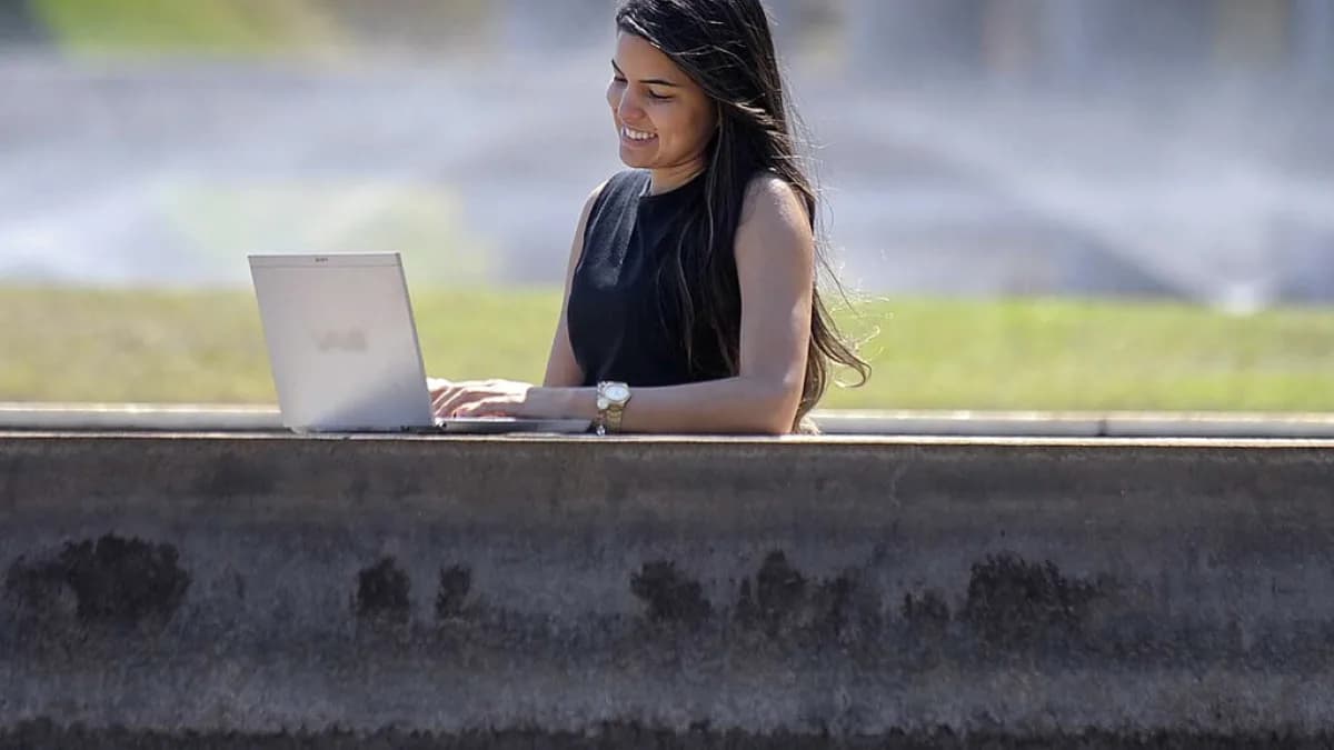 Mulher sorri enquanto usa um notebook ao ar livre