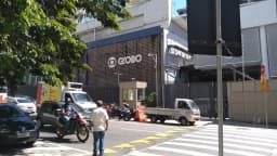 Fachada da sede da TV Globo, com rua, veículos e pessoas ao redor